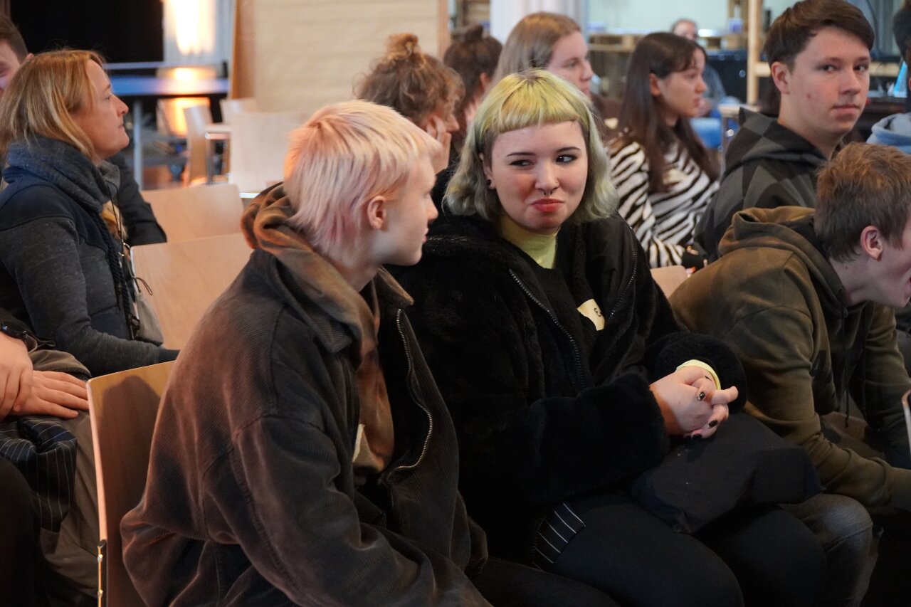 Junge Menschen sitzen in Stuhlreihen und hören zu.